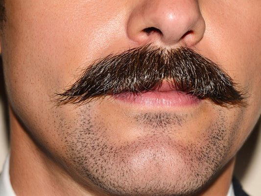 Man with groomed mustache, neutral background.