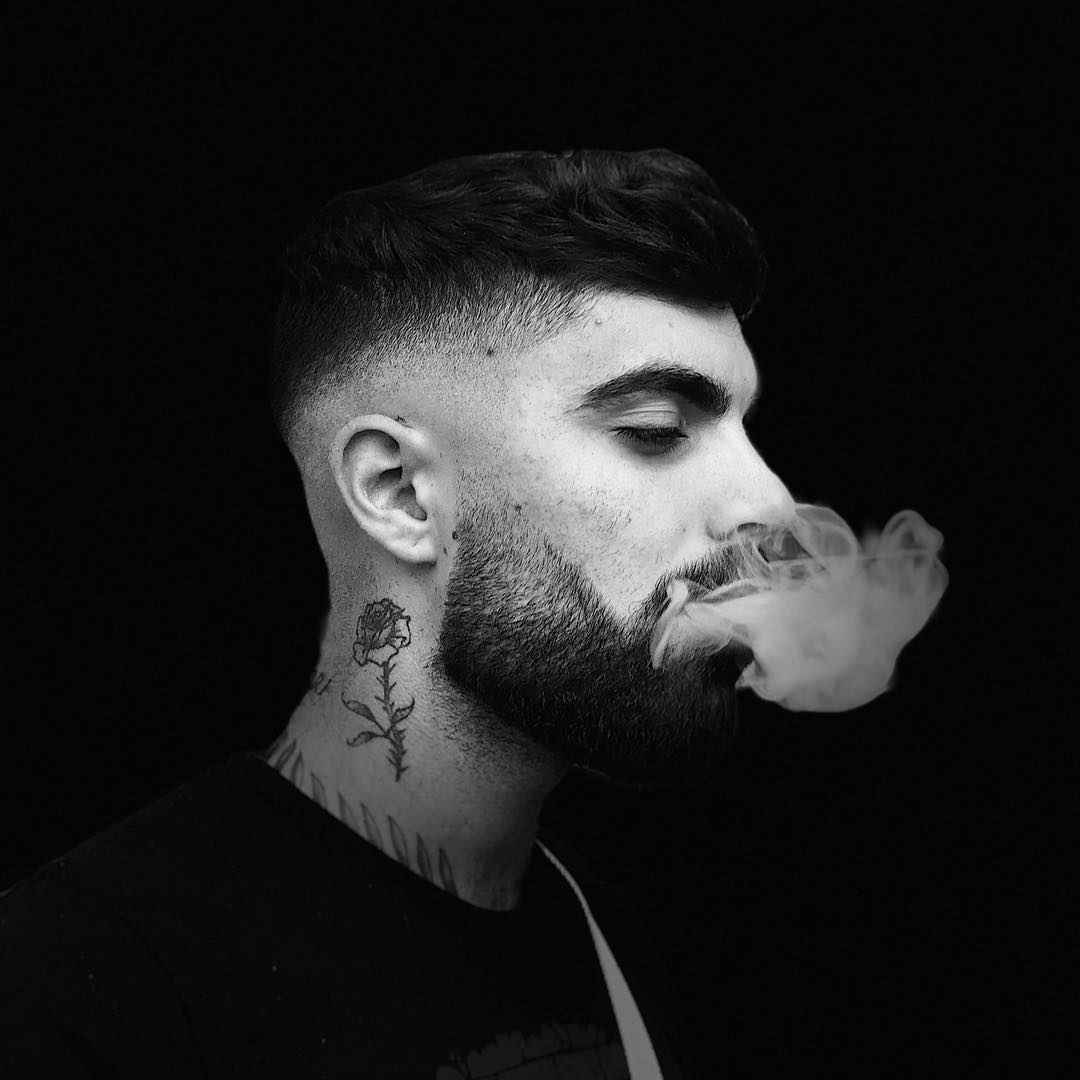 Barber with a clean fade haircut exhaling smoke, showcasing modern grooming style at a Montreal barbershop.