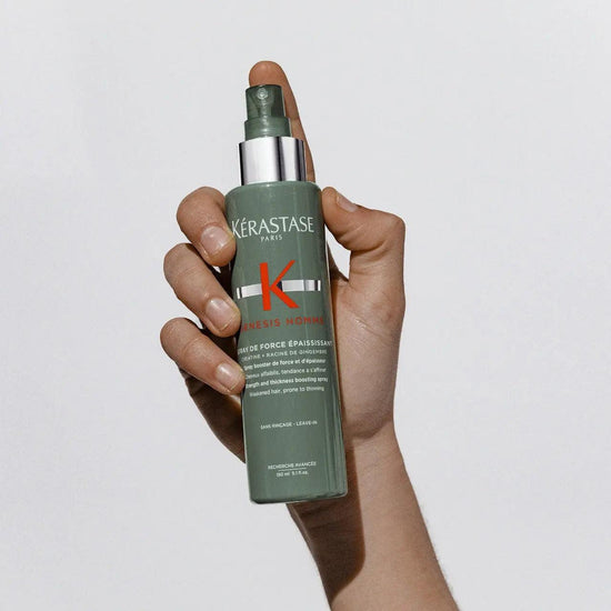 Hand holding Kerastase Genesis Homme Spray de Force Épaississant thickening spray against a white background.