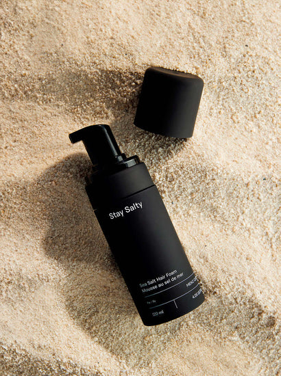 Stay Salty Sea Salt Hair Foam bottle on sandy beach surface for adding body and volume to hair.